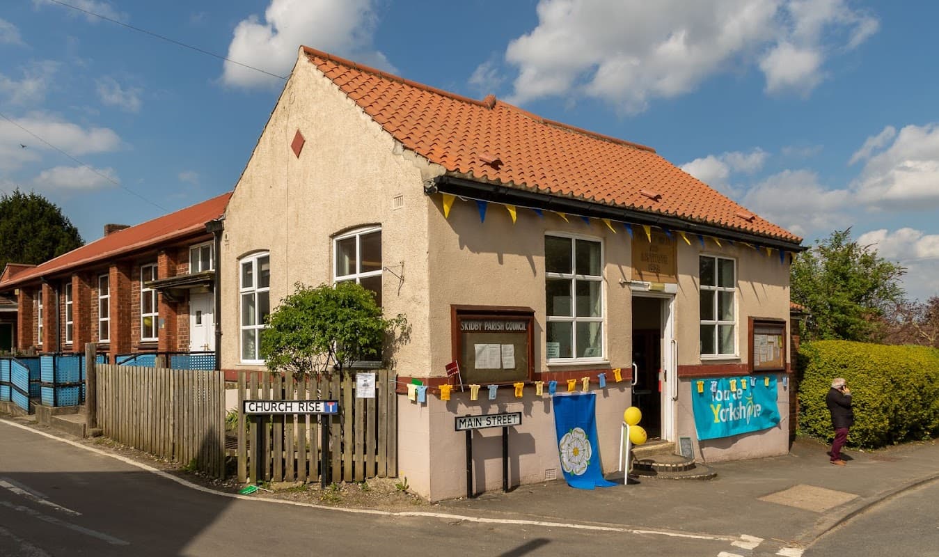 Skidby Parish Council building with colorful bunting, signs for Church Rise and Main Street, and a clear blue sky.