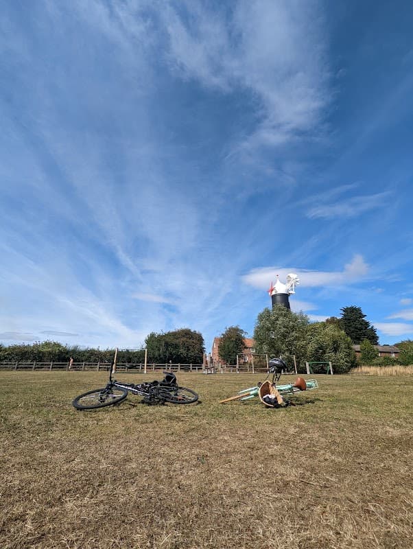Bicycles and playground equipment on grassy field with blue sky and distant windmill in Skidby, Yorkshire.