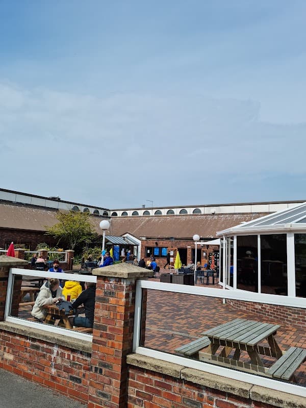 Outdoor seating area at Haven Far Grange Caravan Sales, with people enjoying the sunny day and colorful umbrellas.