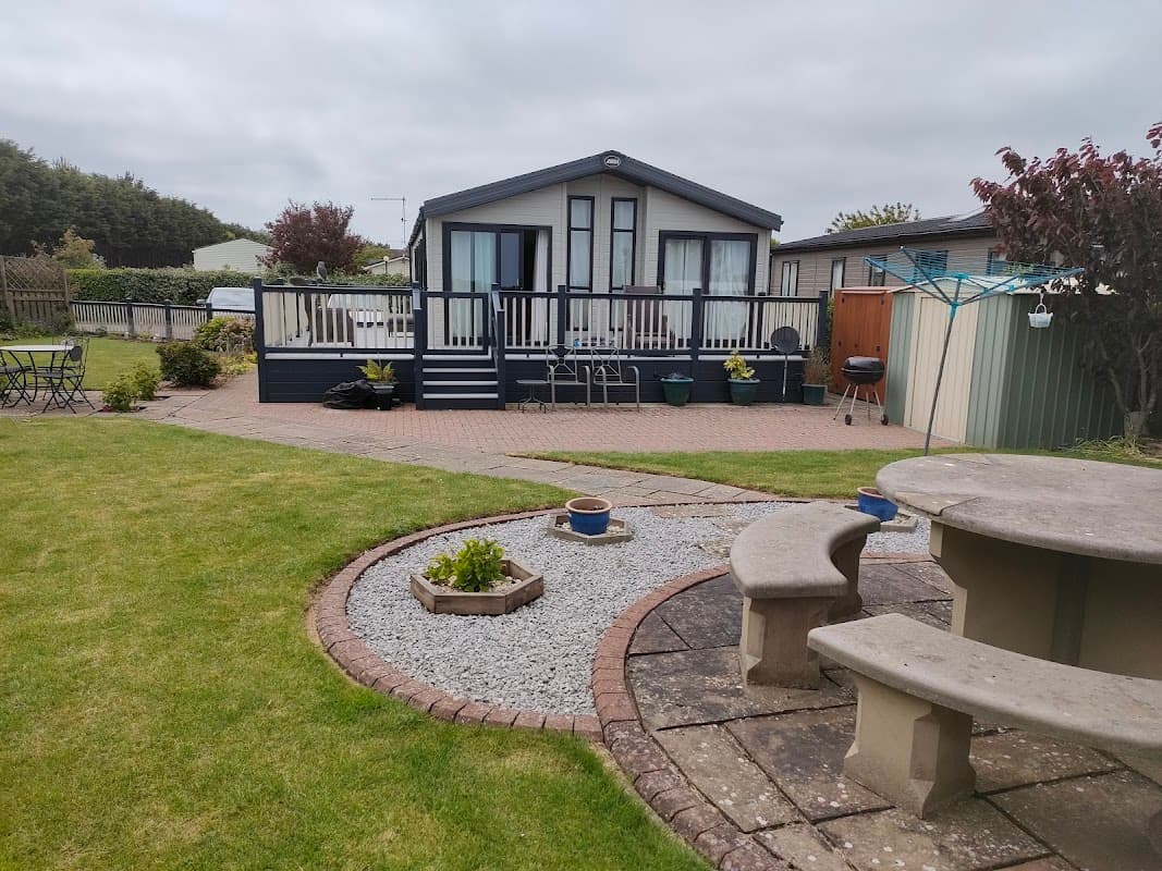Holiday park with a modern cabin, landscaped garden, stone seating area, and gravel pathways in Skipsea, Yorkshire.