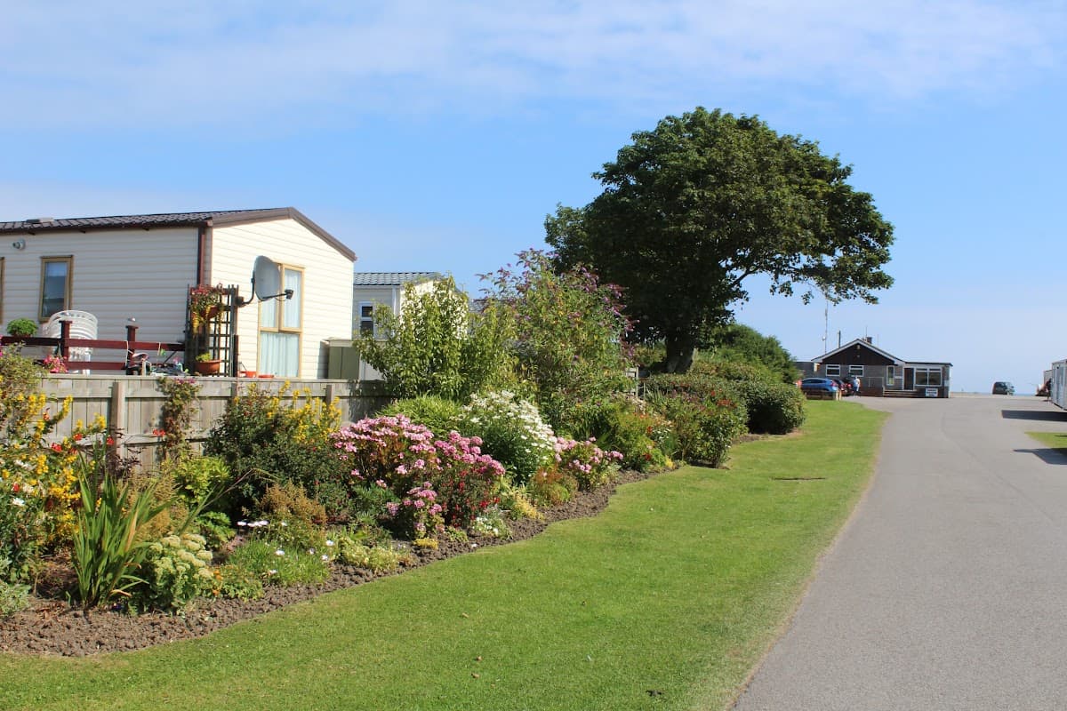 Colorful flower beds line a pathway leading to caravans and a building at Seaside Caravan Park in Skipsea, Yorkshire.