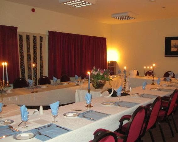 Elegant dining setup with blue napkins, candles, and floral centerpiece in a warmly lit hall. Red curtains in the background.