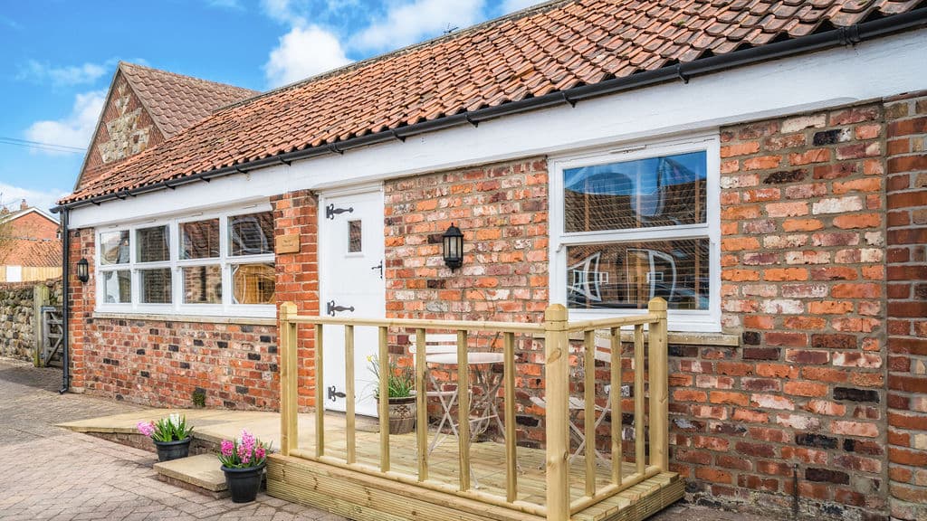 Charming brick building with a wooden deck, potted flowers, and large windows under a blue sky in Skipsea, Yorkshire.