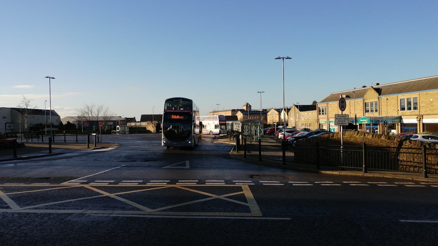 Bus station with a bus at Stand 4, surrounded by buildings and parked cars under a clear blue sky.