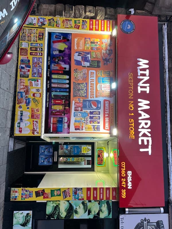 Brightly lit storefront of MINI MARKET with colorful product displays, snacks, and beverages in Skipton, Yorkshire.