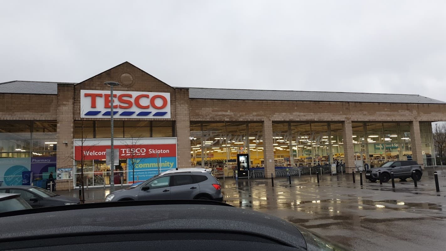 Large Tesco Superstore in Skipton, Yorkshire, with a welcoming sign, visible parking, and cloudy skies.