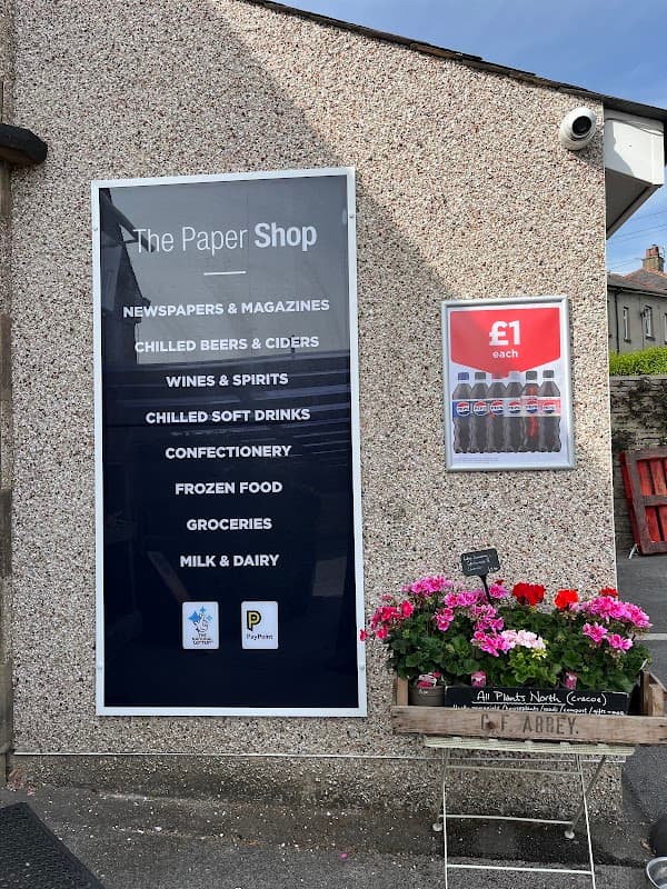 Sign for "The Paper Shop" listing products like newspapers, wines, soft drinks, and flowers in front of the shop.