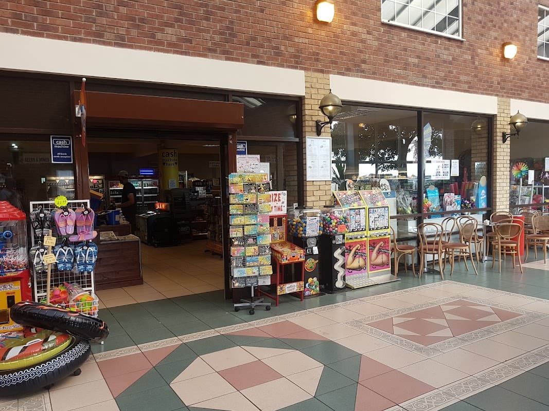 Entrance to Skirlington Supermarket with displays of snacks, toys, and beach items, alongside seating area and checkout.
