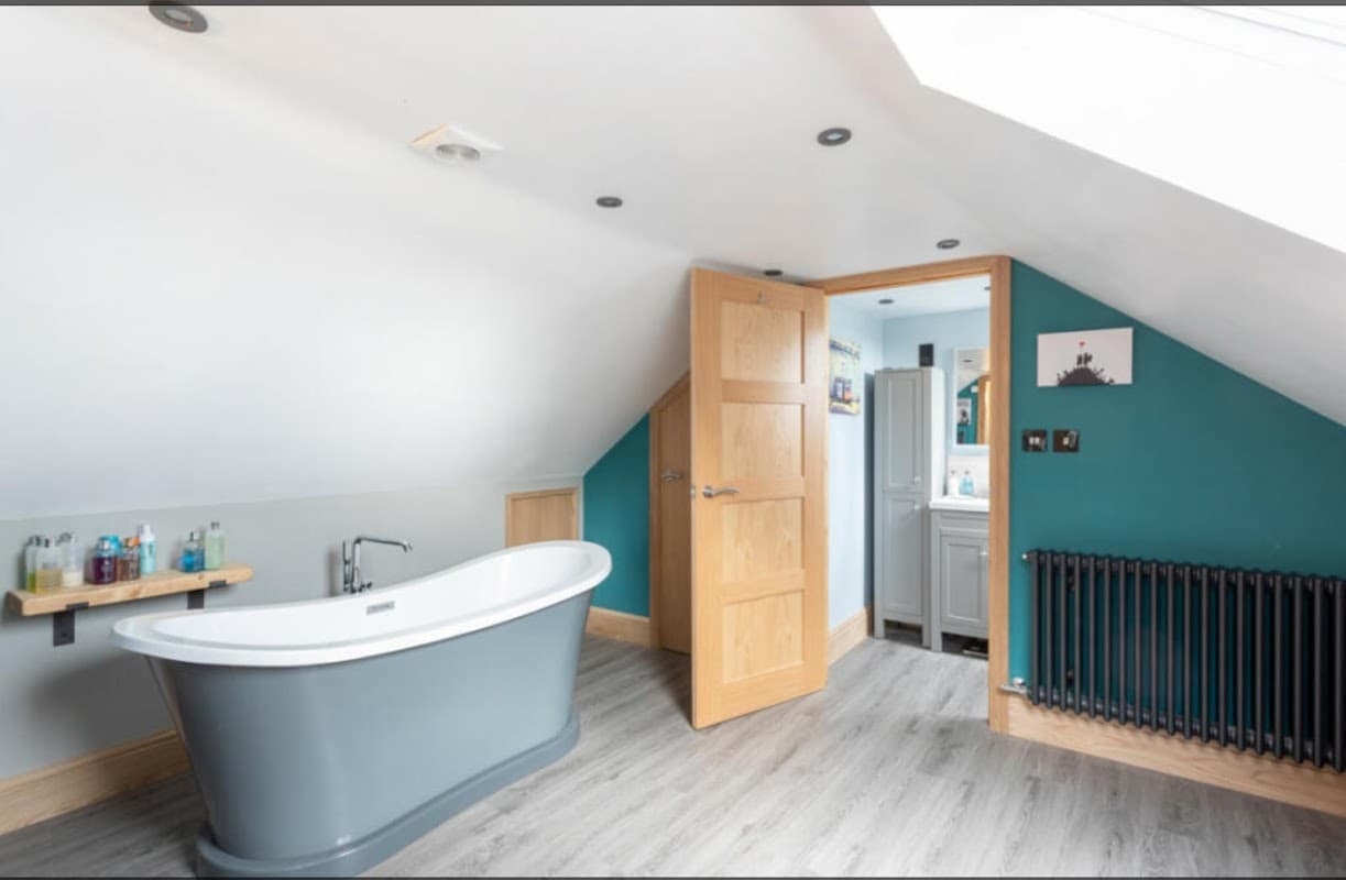 Modern bathroom with a freestanding bathtub, wooden accents, teal walls, and a stylish radiator.