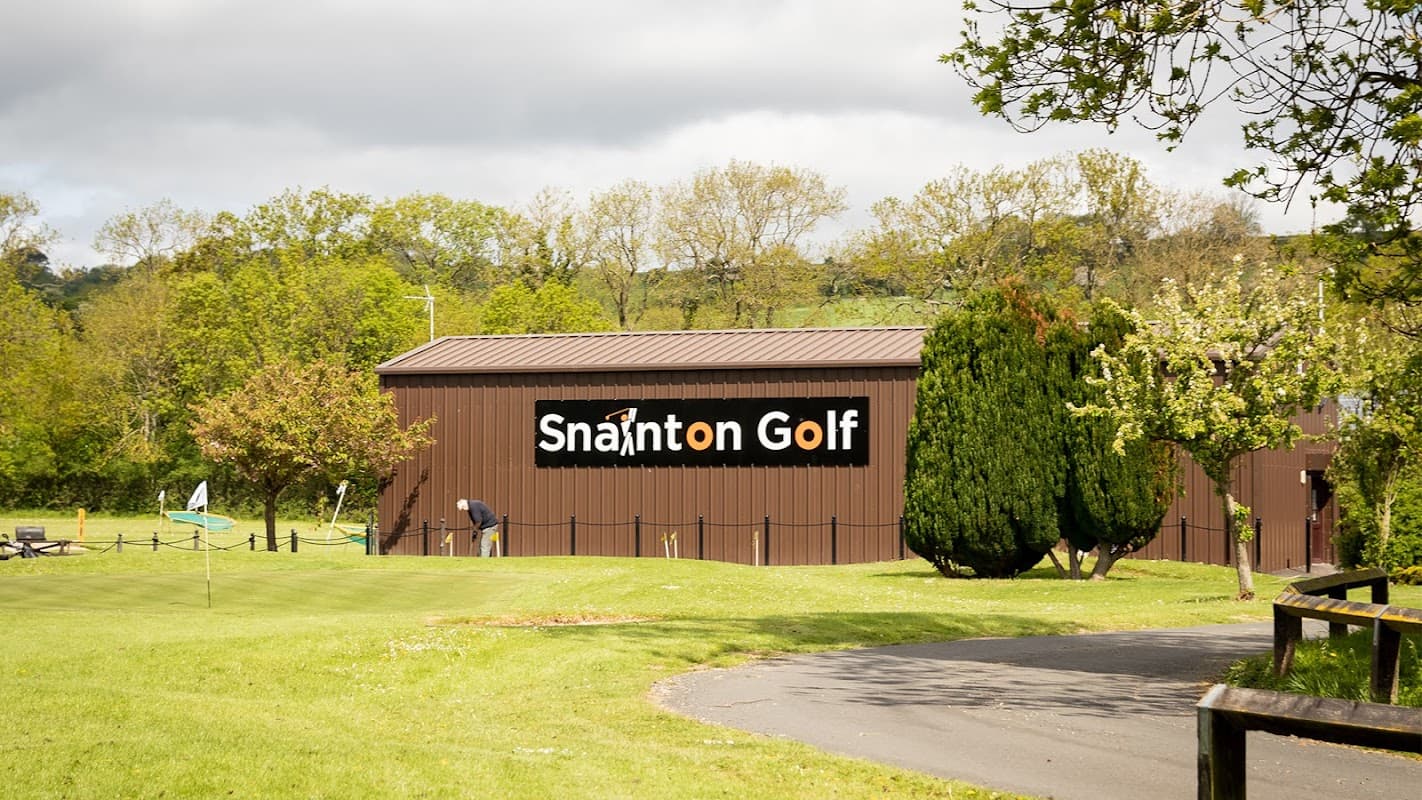 Snainton Golf Centre building with a sign, surrounded by trees and a well-maintained green landscape.