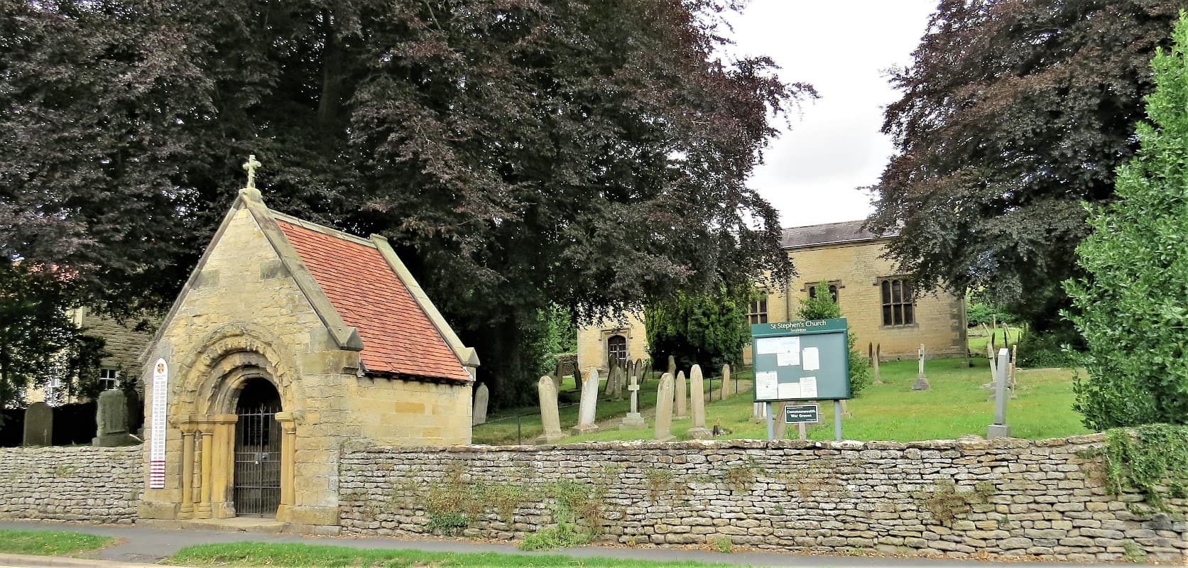 St Stephen's Church with stone walls, gravestones, and lush trees in Snainton, Yorkshire.