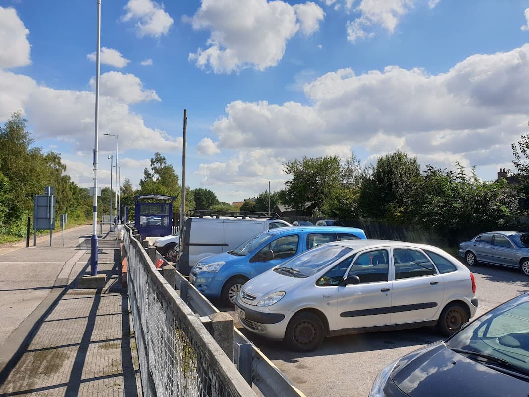 Snaith station car park with several parked cars under a blue sky and fluffy clouds, surrounded by greenery.