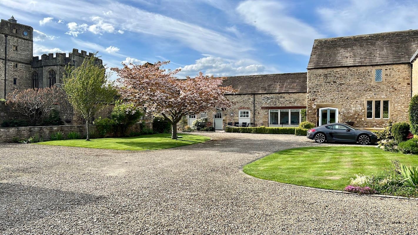 Holiday cottages with a stone exterior, blooming cherry tree, and a car parked on a gravel driveway in Snape, Yorkshire.