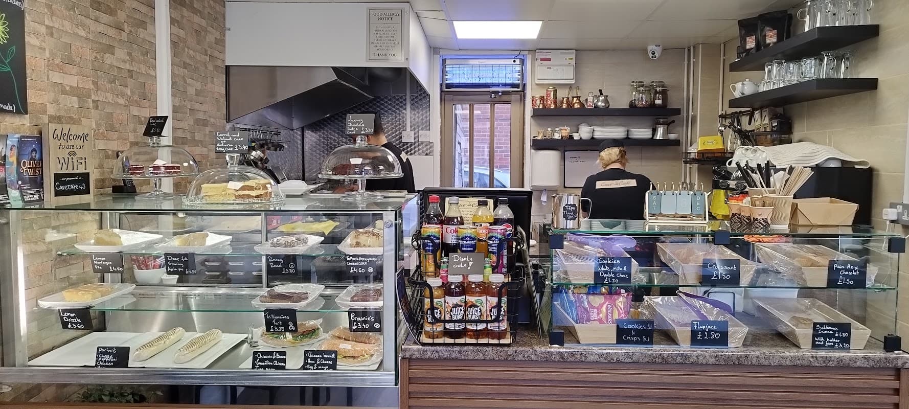 Counter display with cakes, pastries, drinks, and a barista behind the counter in a cozy cafe setting.