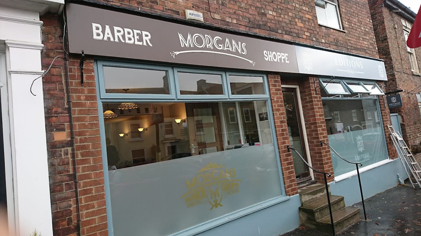 Morgan's Barber Shoppe storefront with large windows and a classic sign, featuring a brick facade and steps leading inside.
