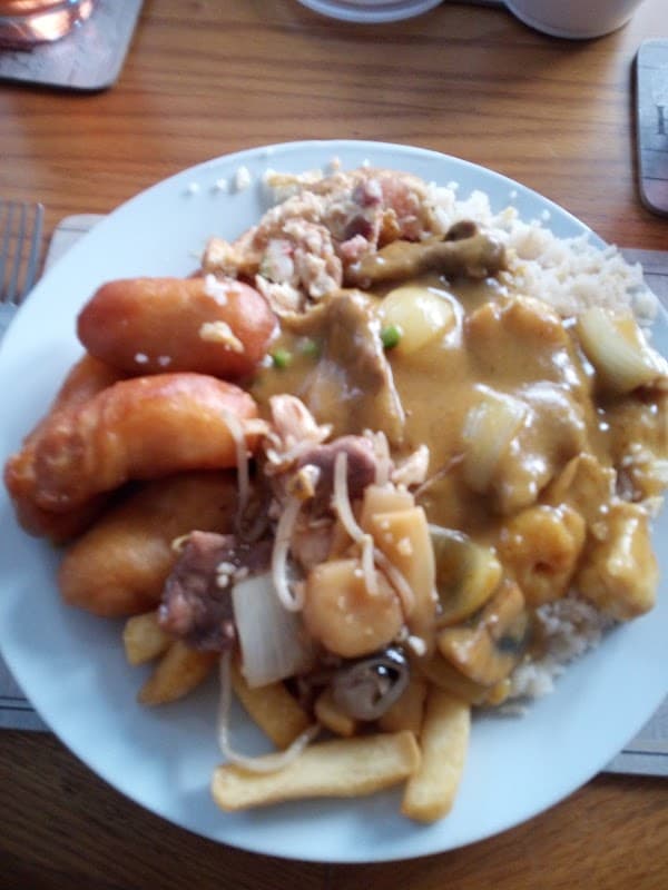 A plate of Chinese takeaway featuring spring rolls, chicken curry, rice, and chips, served on a wooden table.