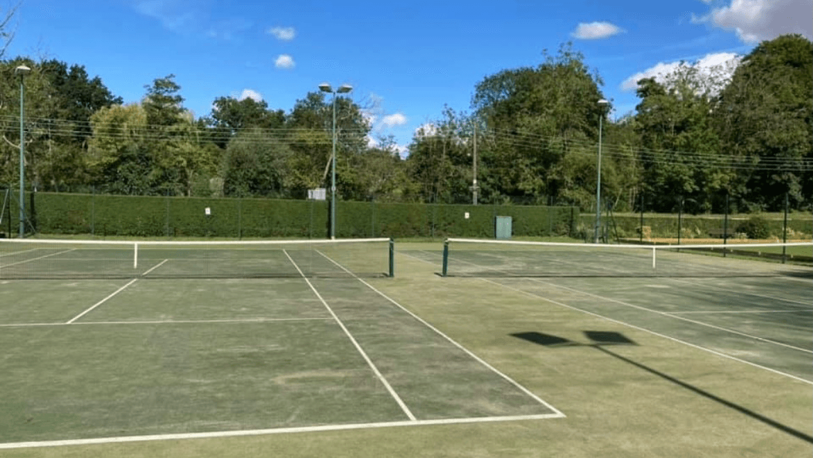 Tennis courts with green fencing, trees in the background, and clear blue skies at South Cave Tennis Club.