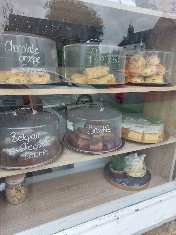 Display of assorted baked goods under glass domes, including scones, flapjack, brownies, and a teapot in the window.