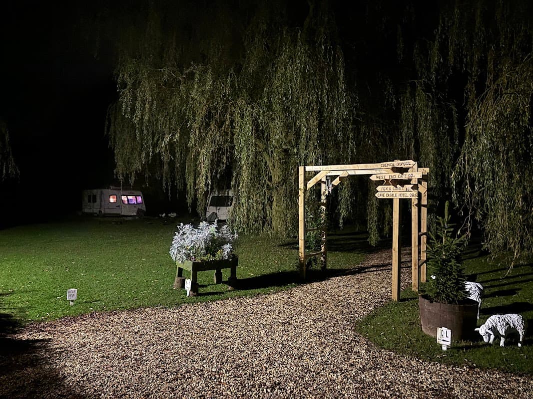 Wooden signpost at night directing to various areas, surrounded by greenery and caravans in a tranquil setting.