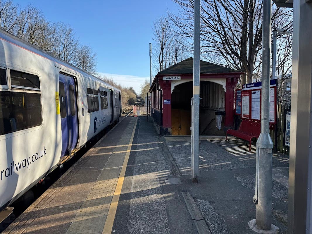 Lockwood Station platform with a train, benches, a ticket booth, and trees lining the background in South Crosland, Yorkshire.