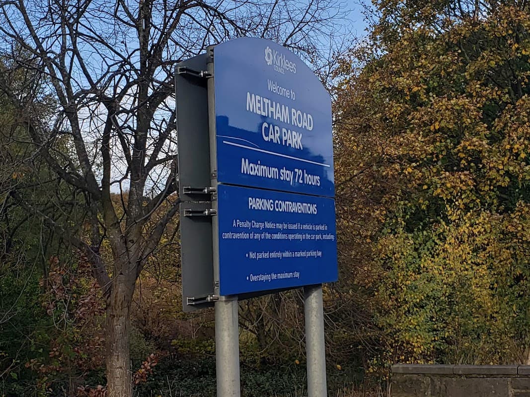 Sign for Meltham Road Car Park with parking regulations and maximum stay details, surrounded by trees in autumn colors.
