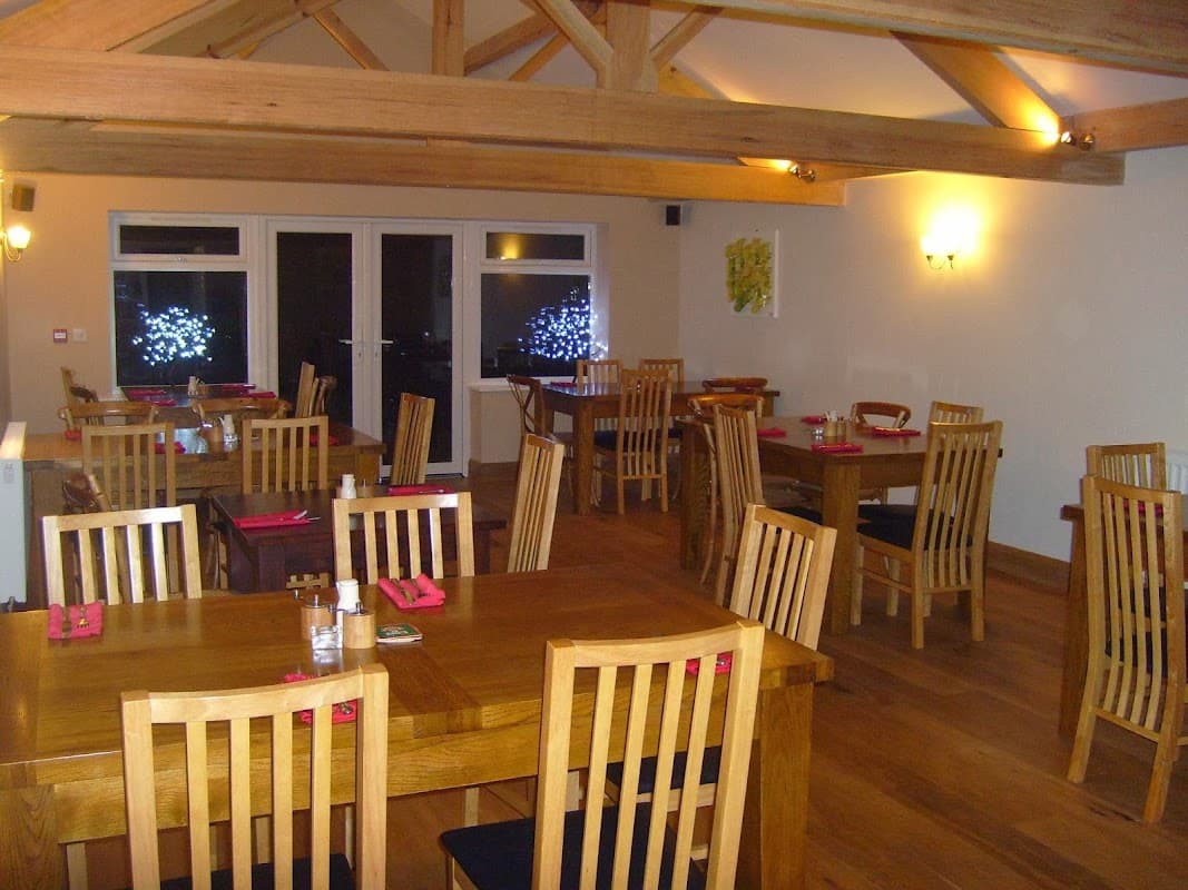 Cozy cafe interior with wooden tables, chairs, and warm lighting; large windows overlook a softly lit outdoor area.