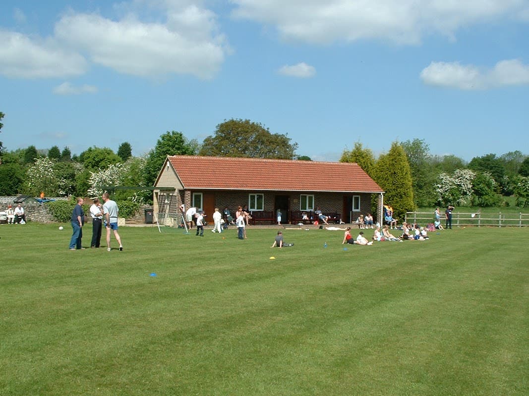 South Milford Cricket Club with a building, green field, and people enjoying outdoor activities on a sunny day.