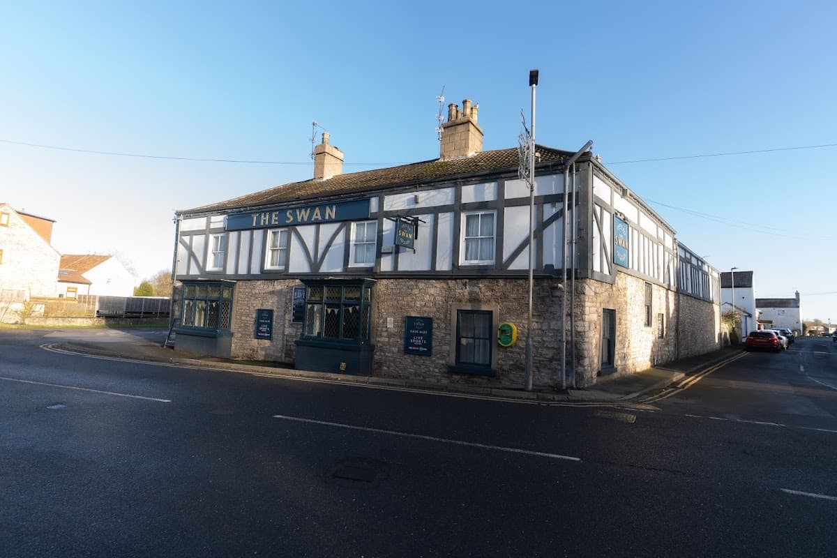Historic building with a sign reading "The Swan," featuring a mix of stone and timber architecture in South Milford.