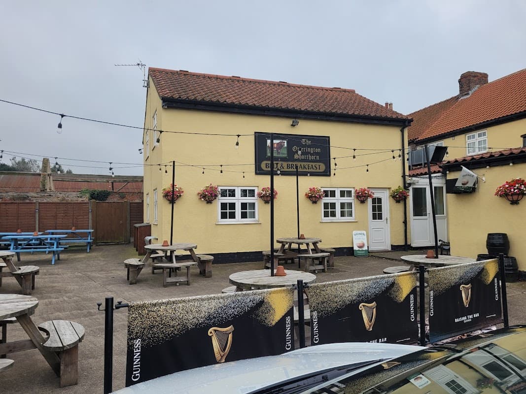 Yellow bar building with a sign, outdoor seating, flower baskets, and a Guinness banner in South Otterington, Yorkshire.