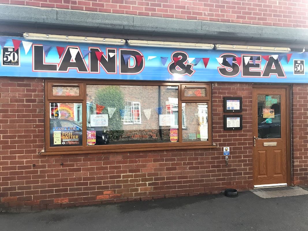 Brightly colored sign reading "LAND & SEA" above a brick restaurant facade with windows and promotional posters.