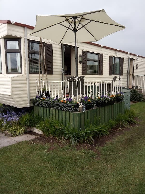 Caravan with a white umbrella, surrounded by flower beds and greenery, set in a grassy area at Sowerby Caravan Park.