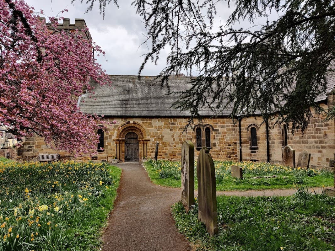 St Oswald's Church surrounded by blooming cherry trees and daffodils, with a stone path leading to the entrance.