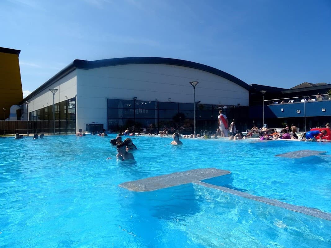 Sunny day at Alpamare UK, featuring a large outdoor pool with swimmers and sunbathers enjoying the water.
