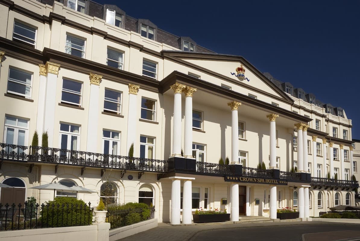 Elegant white facade of Crown Spa Hotel, featuring grand columns and ornate detailing under a clear blue sky.