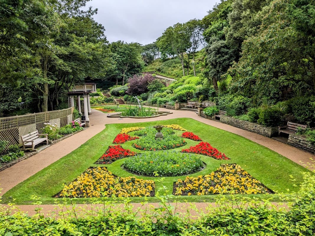 Lush garden with vibrant flowerbeds, pathways, benches, and greenery under a cloudy sky in Spa Bridge, Yorkshire.