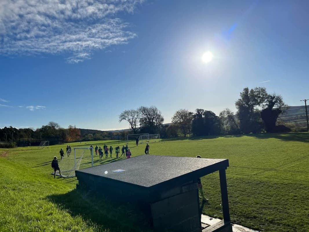 Youth football players practice on a green field under a clear blue sky with the sun shining brightly.