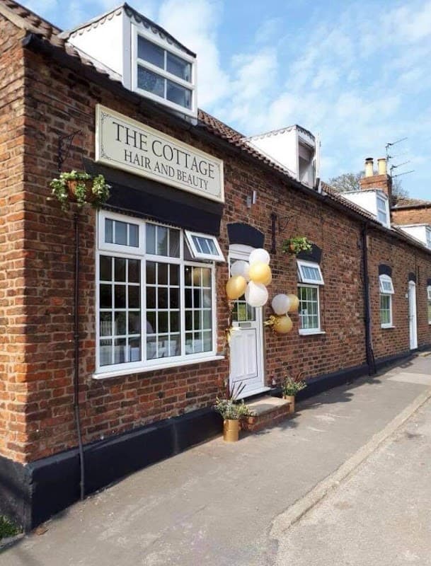 Brick building with large windows, "The Cottage Hair & Beauty" sign, and decorative balloons outside.