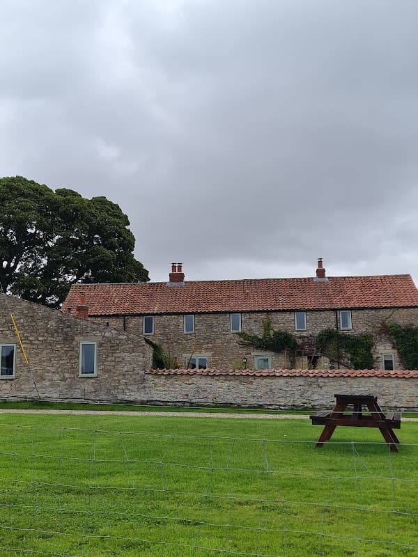 Stone cottages with red roofs, lush green lawn, and a large tree under a cloudy sky in Sproxton, North Yorkshire.