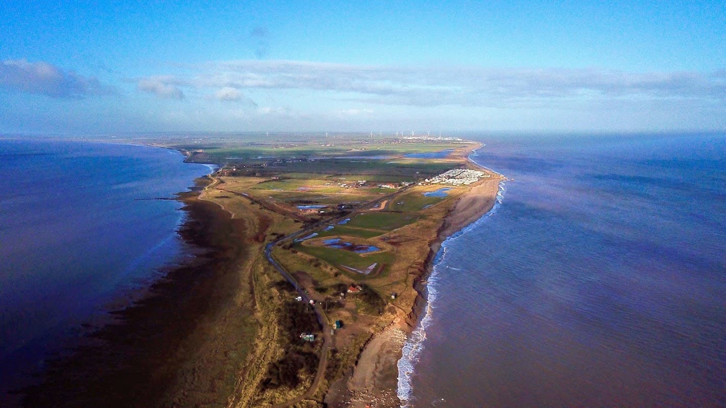 Aerial view of Spurn Point, showcasing sandy beaches, green fields, and coastal waters under a clear blue sky.