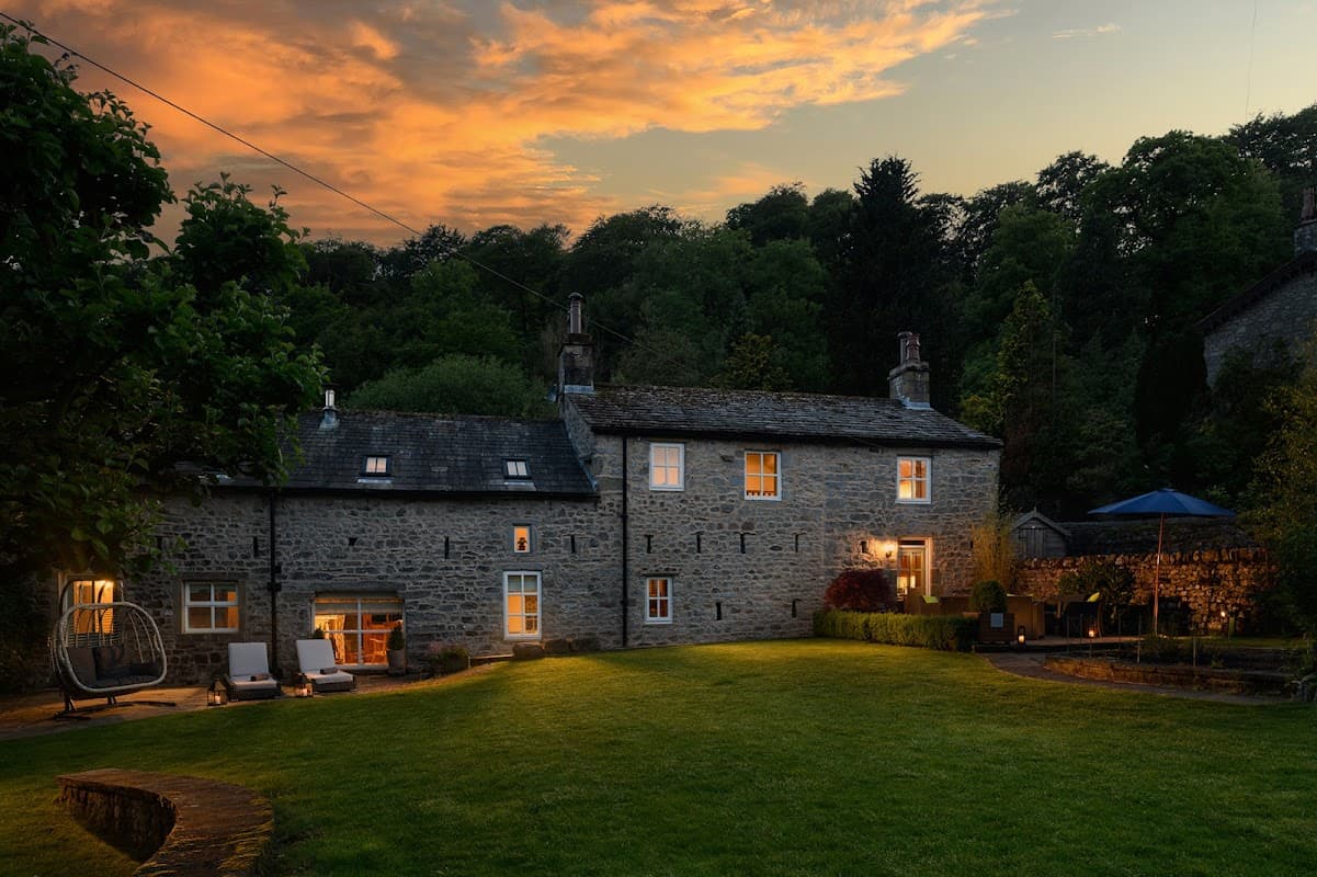 Carrholme Cottage surrounded by lush greenery, with a sunset sky, outdoor seating, and a cozy atmosphere.
