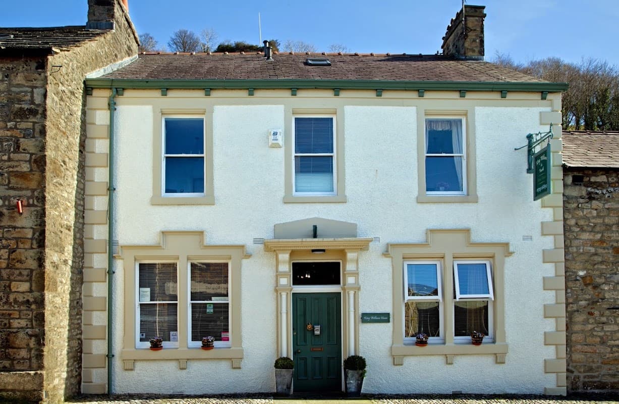 Charming guest house with white exterior, green door, and window boxes, set in a stone village in North Yorkshire.