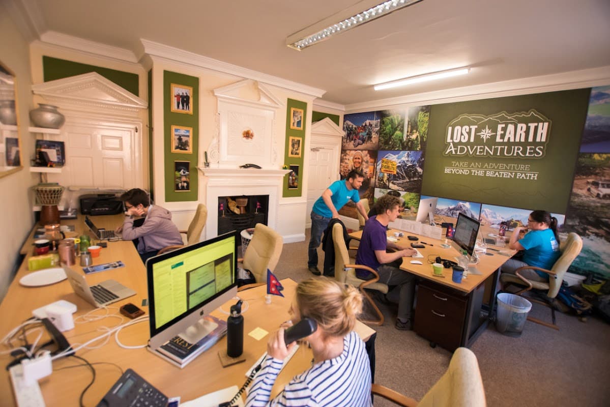 Office scene at Lost Earth Adventures with staff at desks, engaging in calls, and adventure-themed wall decor.
