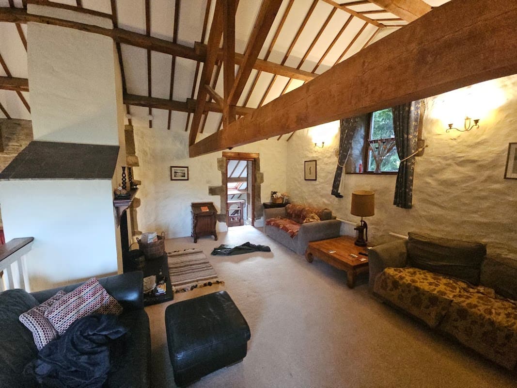 Cozy living area with high wooden beams, comfortable sofas, a coffee table, and natural light from windows.