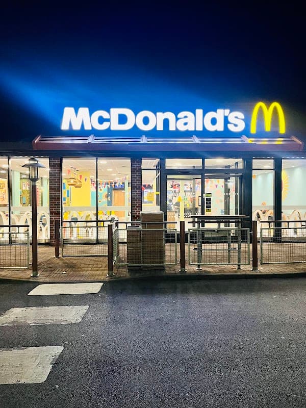McDonald's restaurant exterior at night, featuring bright signage and large windows with colorful interior decor.