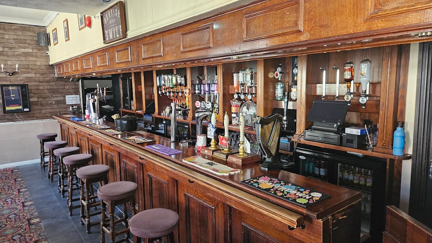 Wooden bar with stools, beer taps, and a variety of drinks displayed; warm, inviting atmosphere in a cozy pub setting.