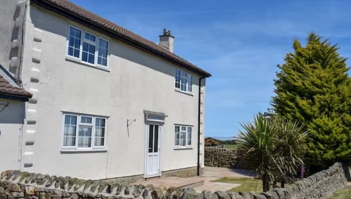 White holiday cottage with a stone wall, surrounded by greenery and a clear blue sky in Staintondale, Yorkshire.
