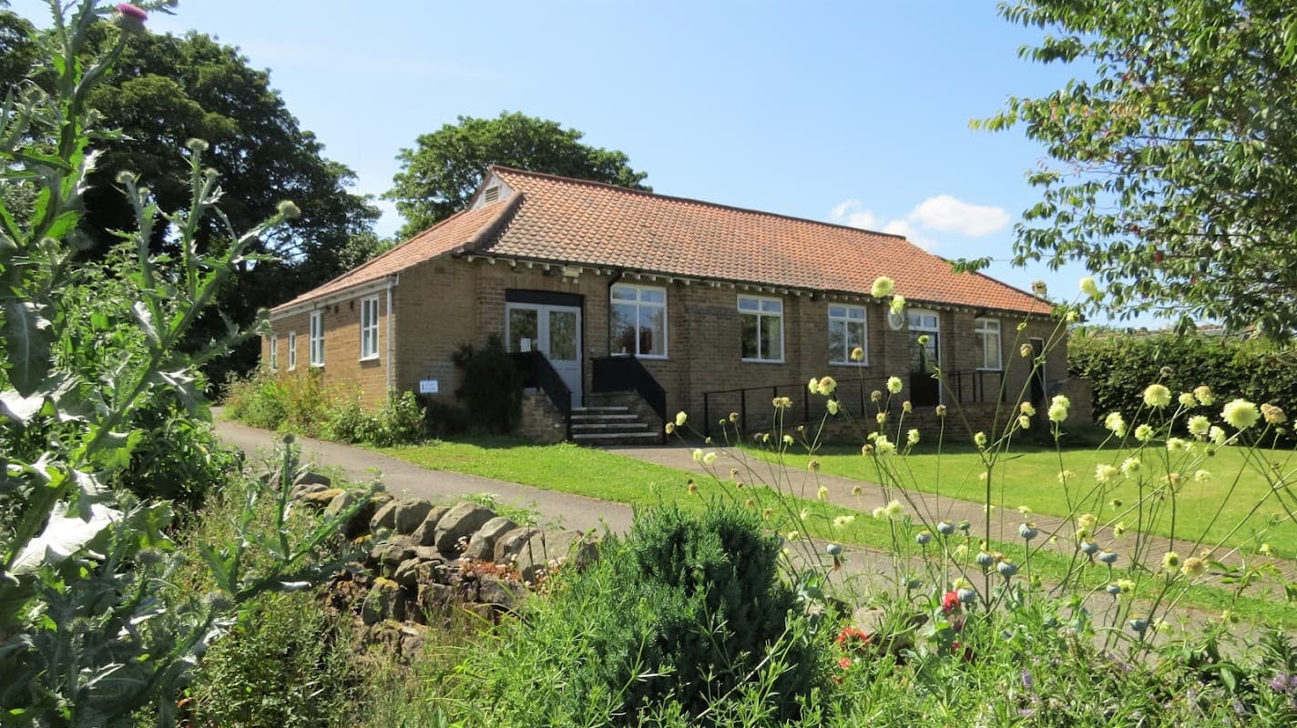 Staintondale Post Office, a brick building with a red-tiled roof, surrounded by greenery and flowers on a sunny day.