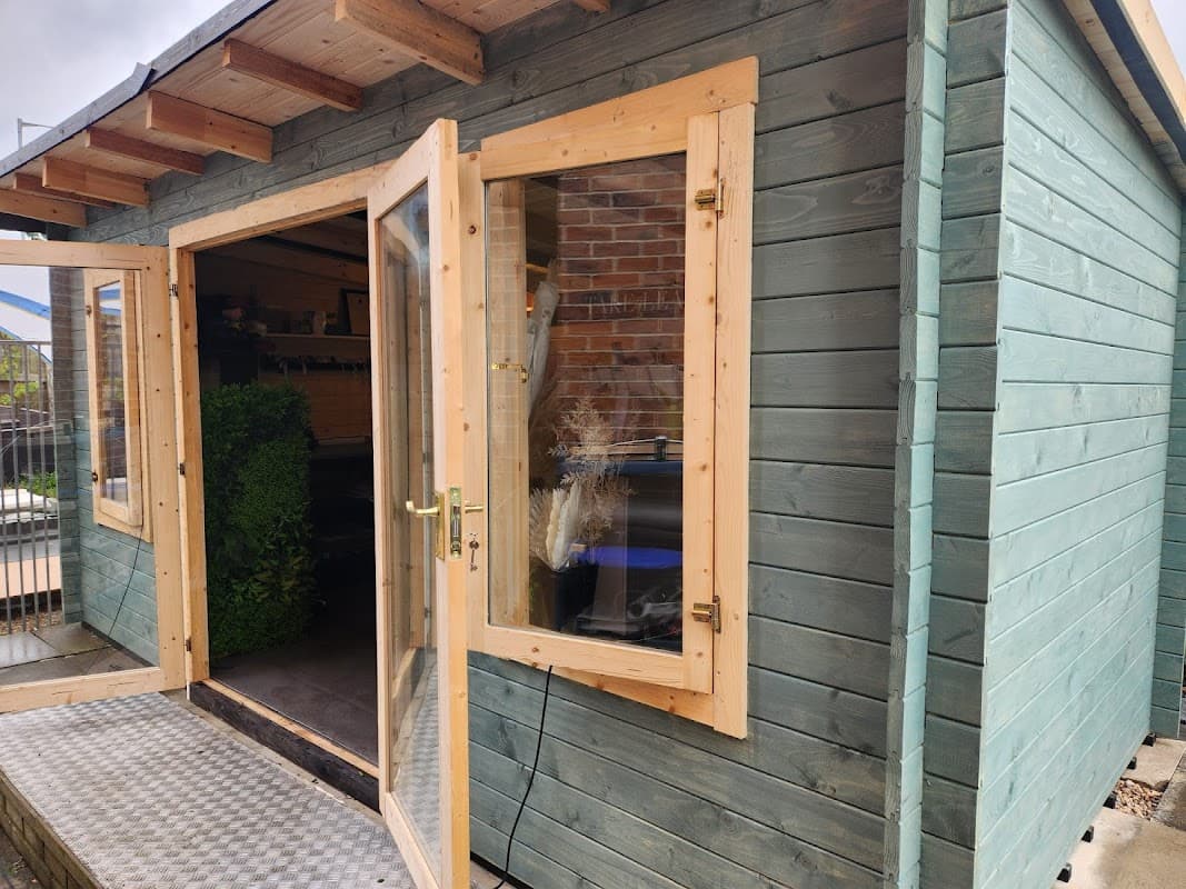 Quaint wooden florist shop with large glass doors and a green exterior, surrounded by potted plants and a welcoming entrance.
