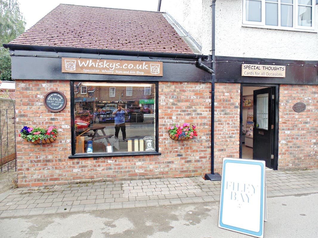 Brick exterior of Whiskys shop with flower boxes, signs for whisky and cards, and a sandwich board outside.