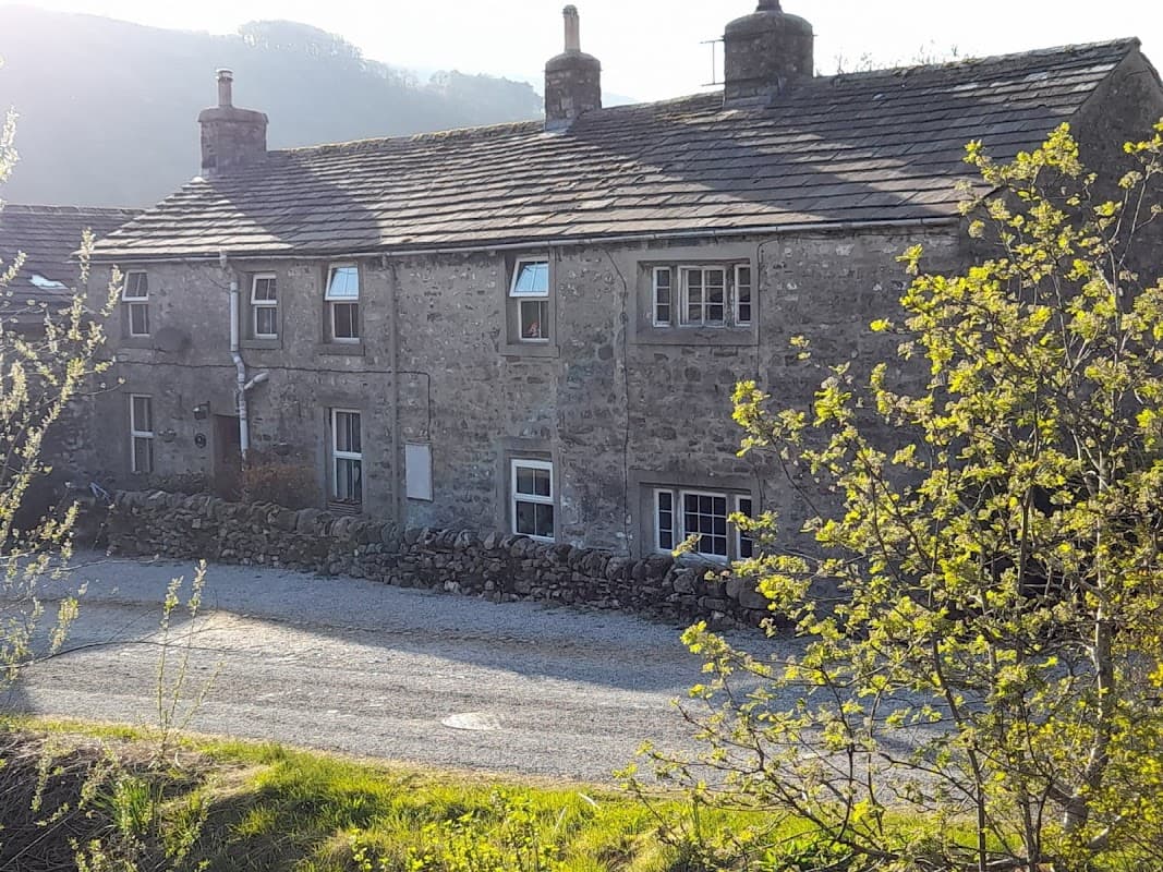 Stone cottage surrounded by greenery, gravel driveway, and scenic hills in the background, located in Starbotton, Yorkshire.